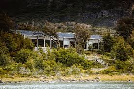 Modern hotel with contemporary wooden exterior nestled against snow-capped mountains, reflecting in the tranquil waters of Grey Lake in Patagonia