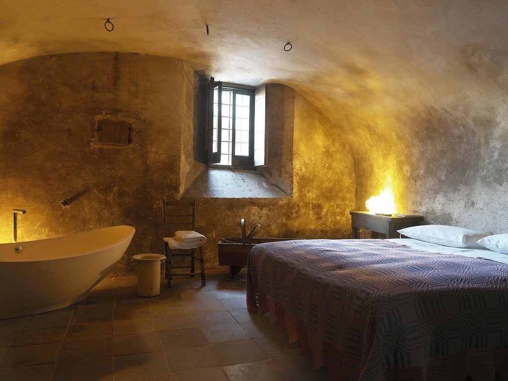 Rustic Italian hotel room with stone walls, antique wooden furnishings, and a panoramic view of medieval bell tower through arched window