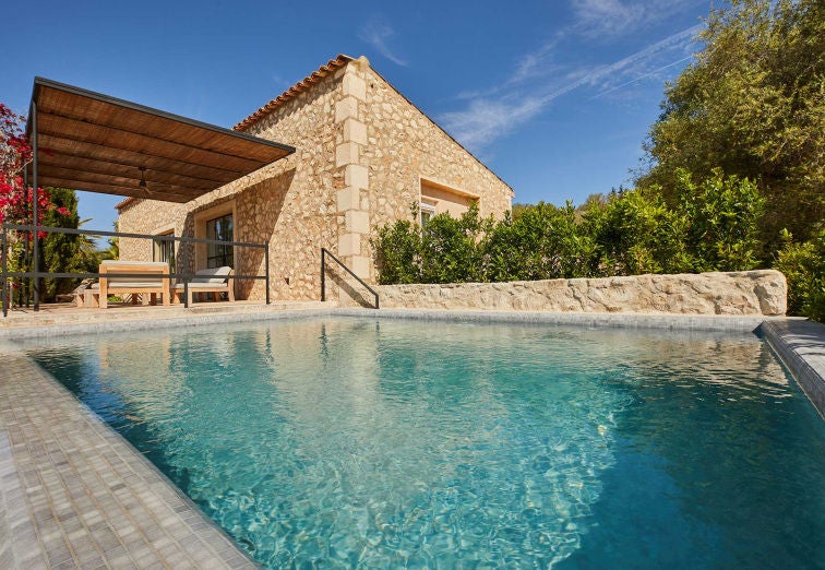 Elegant hotel suite with exposed wooden beams, white textured walls, and minimalist decor overlooking Mediterranean countryside views