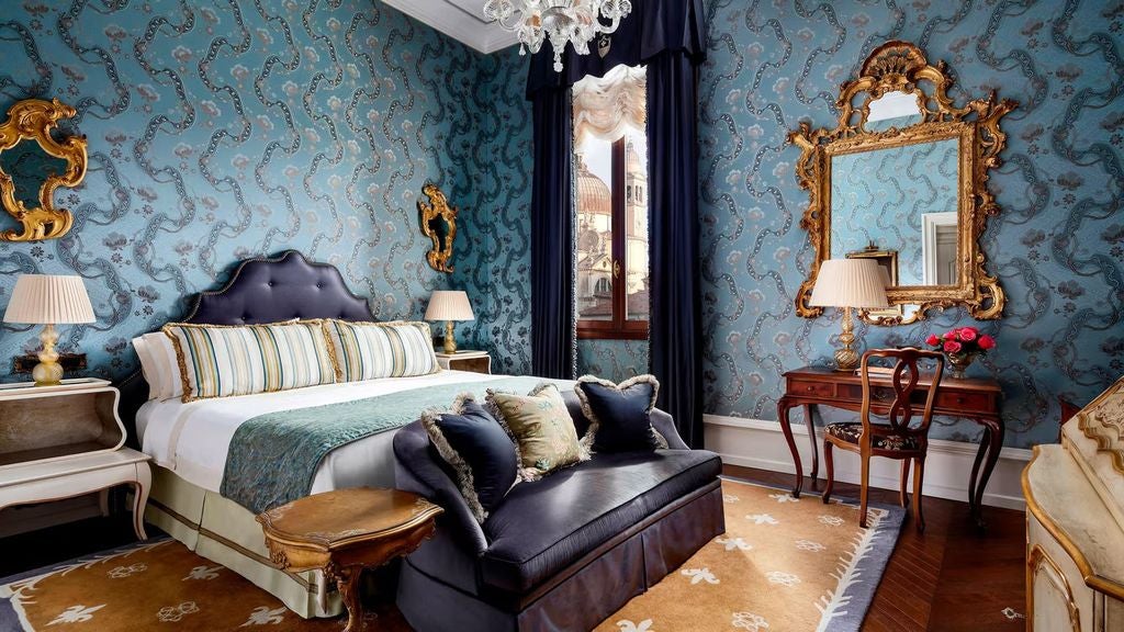 Opulent Venetian hotel room with velvet furniture, gilded mirrors, Murano glass chandelier, and ornate wall panels overlooking Grand Canal