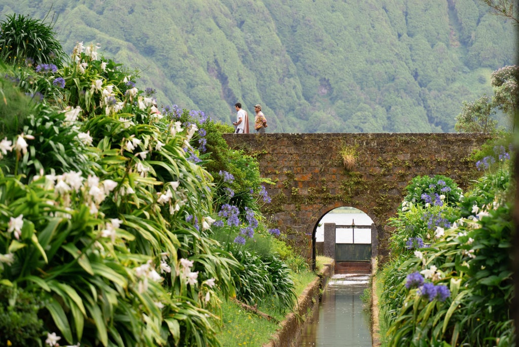 Verdant crater lake nestled between lush green slopes of Sete Cidades, São Miguel, with misty volcanic landscape and luxurious azure water reflections