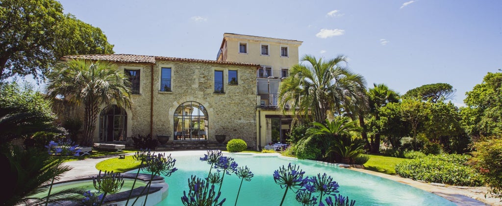 Elegant French château hotel with stone facade, surrounded by manicured gardens and vineyards under a warm sunset sky