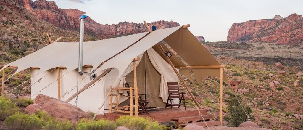 Luxurious glamping tents nestled against rugged red rock cliffs of Zion National Park, showcasing elegant canvas shelters with mountain backdrop at sunset