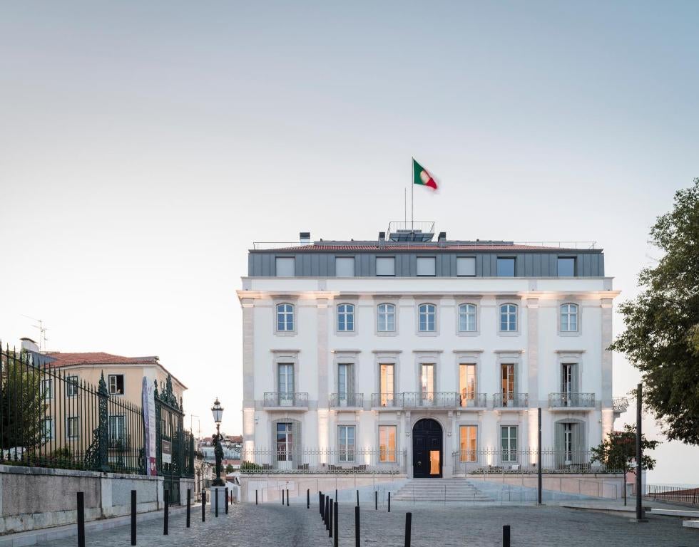 Elegant 18th-century palace hotel with white facade, ornate balconies, and wrought-iron details overlooking Lisbon's historic quarter.