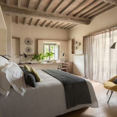 Elegant Tuscan hotel room with panoramic countryside view, rustic wood furnishings, and soft natural light streaming across luxurious linens