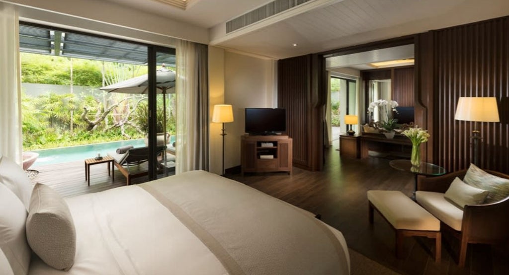 Spacious villa bedroom with king bed, floor-to-ceiling windows, wooden decor, and direct pool access overlooking Phuket's tropical forest