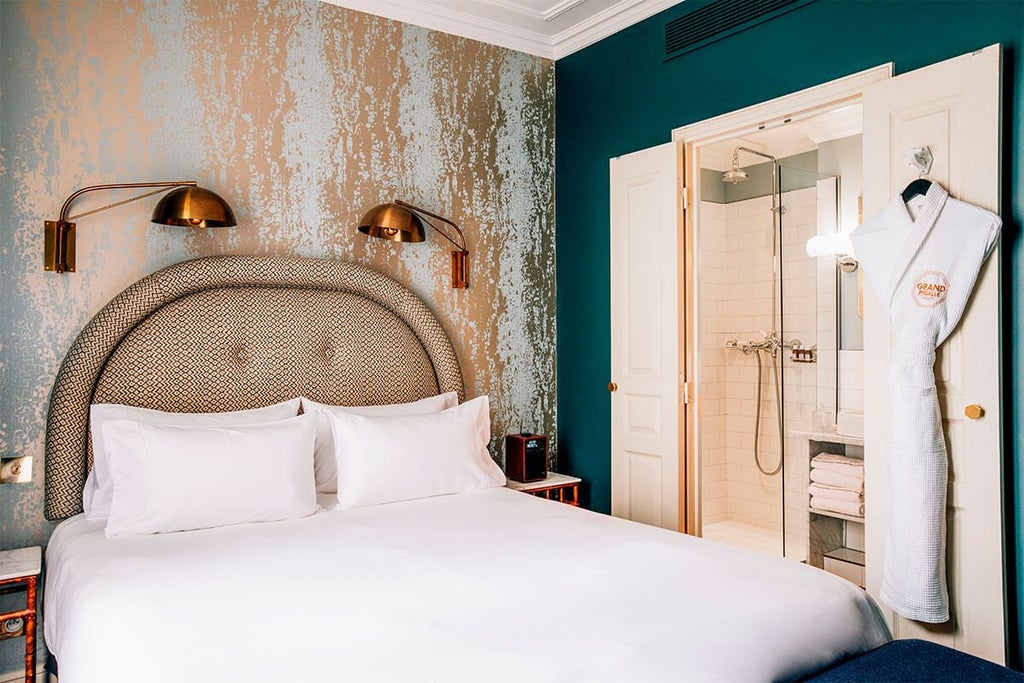 Elegant Parisian hotel room with plush king bed, soft neutral tones, vintage-inspired decor, and large windows overlooking charming street in Grand Pigalle Hotel