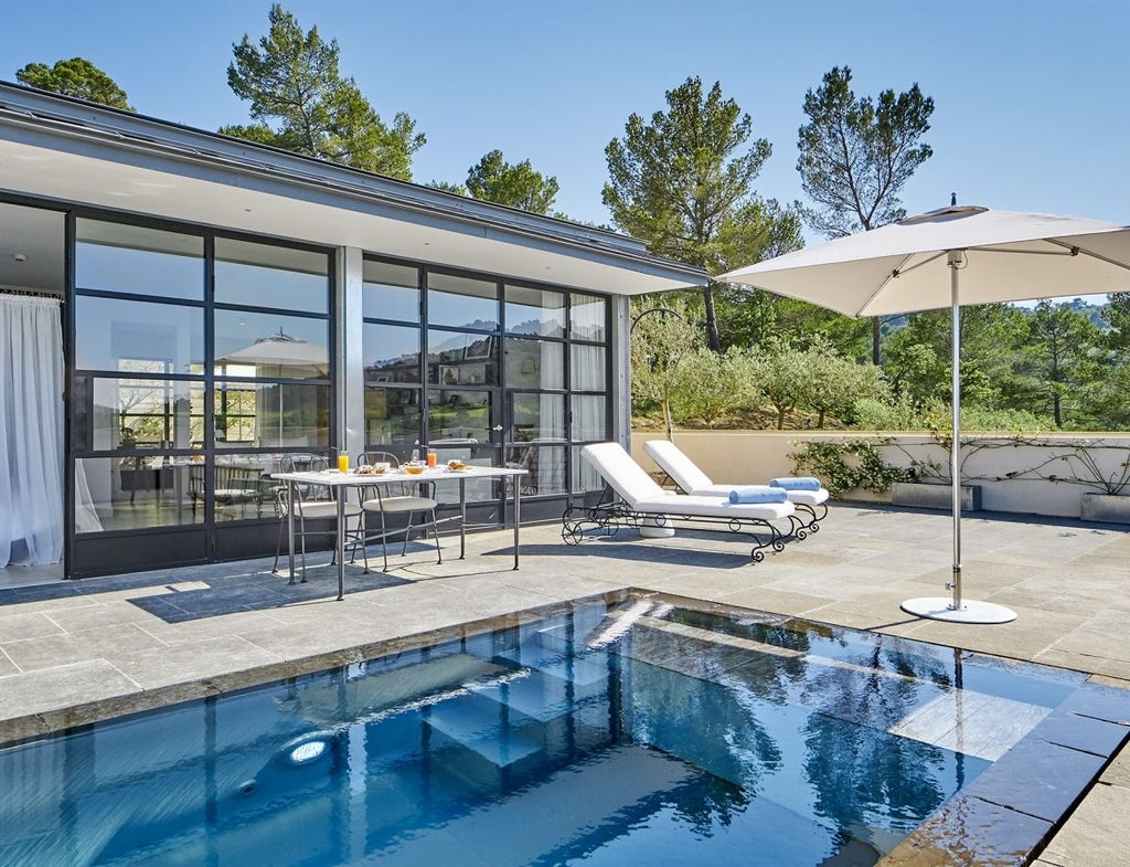 Modern luxury villa suite with private infinity pool overlooking scenic French countryside and mountains at sunset through floor-to-ceiling windows