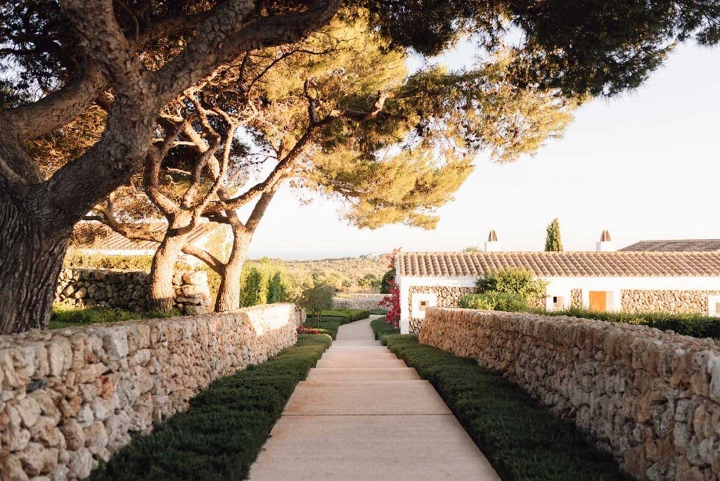 Whitewashed luxury Menorcan farmhouse hotel with stone walls, lavender fields, and rustic Mediterranean elegance against scenic countryside backdrop