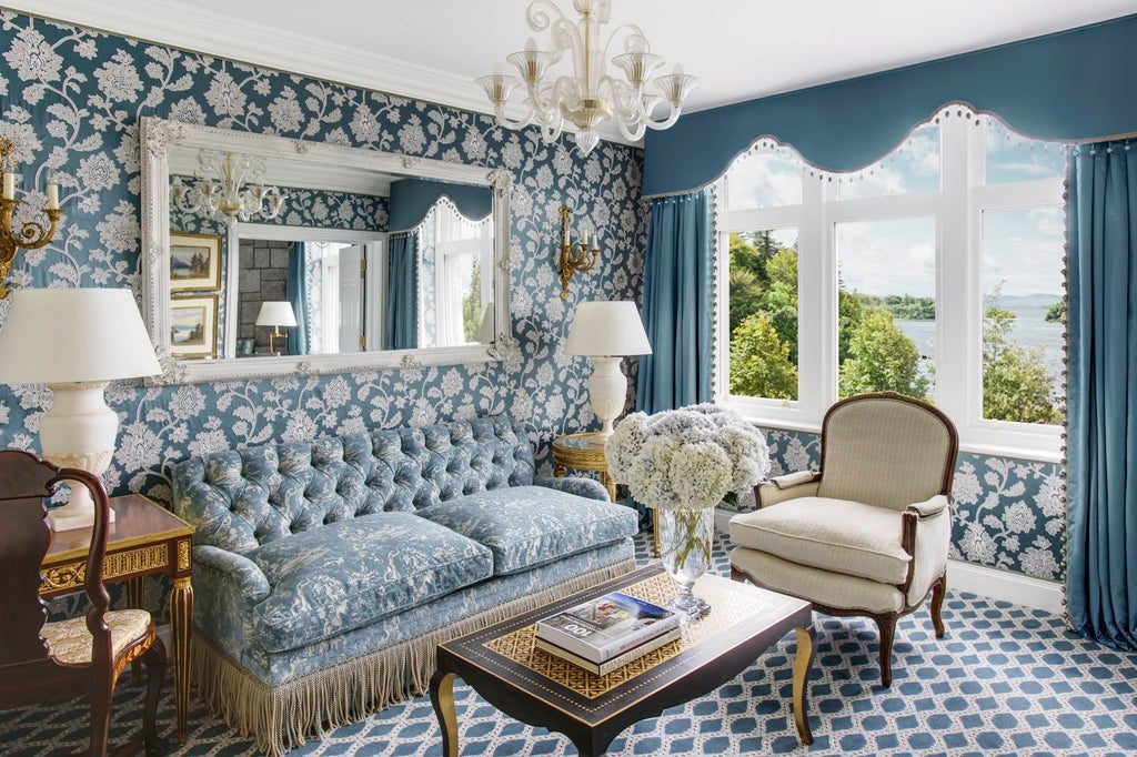 Elegant suite at Ashford Castle featuring ornate gold-framed mirrors, antique furniture, crystal chandelier and plush king bed with canopy