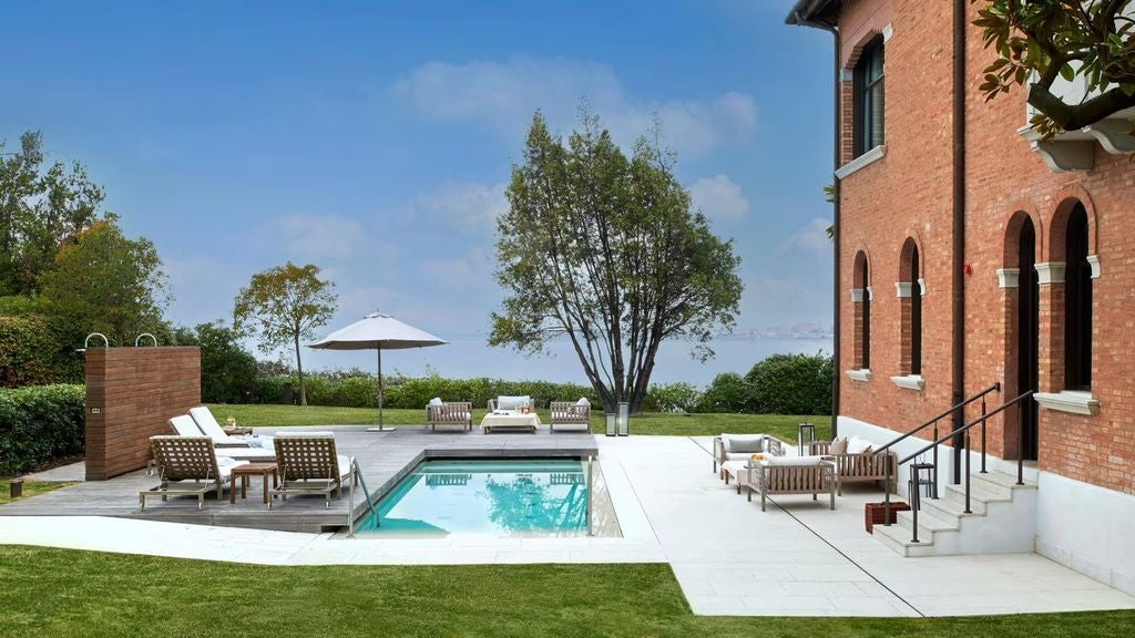 Luxurious hotel villa with private pool overlooking Venice lagoon, featuring elegant outdoor loungers and manicured gardens.