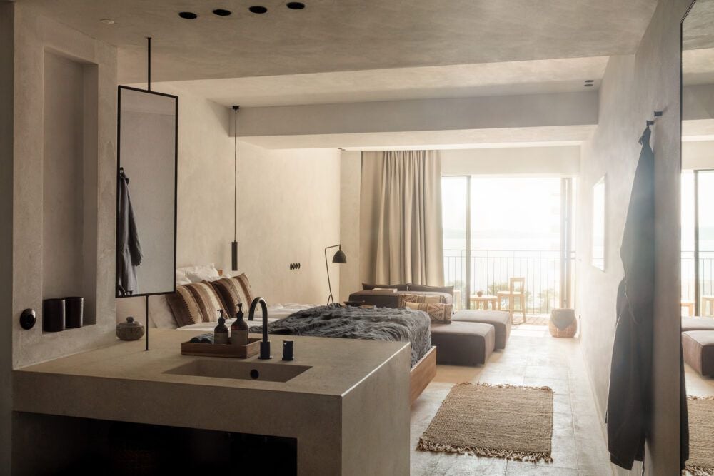 Elegant white-washed Deluxe Room at OKU Ibiza, featuring minimalist design, crisp linens, wooden accents, and a serene Mediterranean view