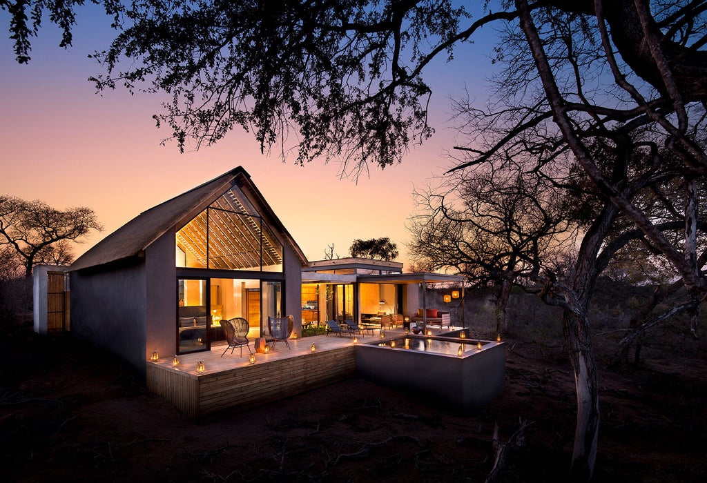 Modern luxury villa suite with private plunge pool overlooking African savanna, featuring floor-to-ceiling glass walls and wooden deck