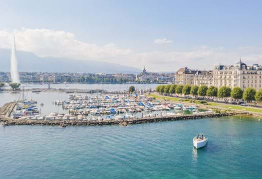 Luxurious lakeside hotel The Woodward in Geneva, Switzerland, with classic Belle Époque architecture and snow-capped Alps in background