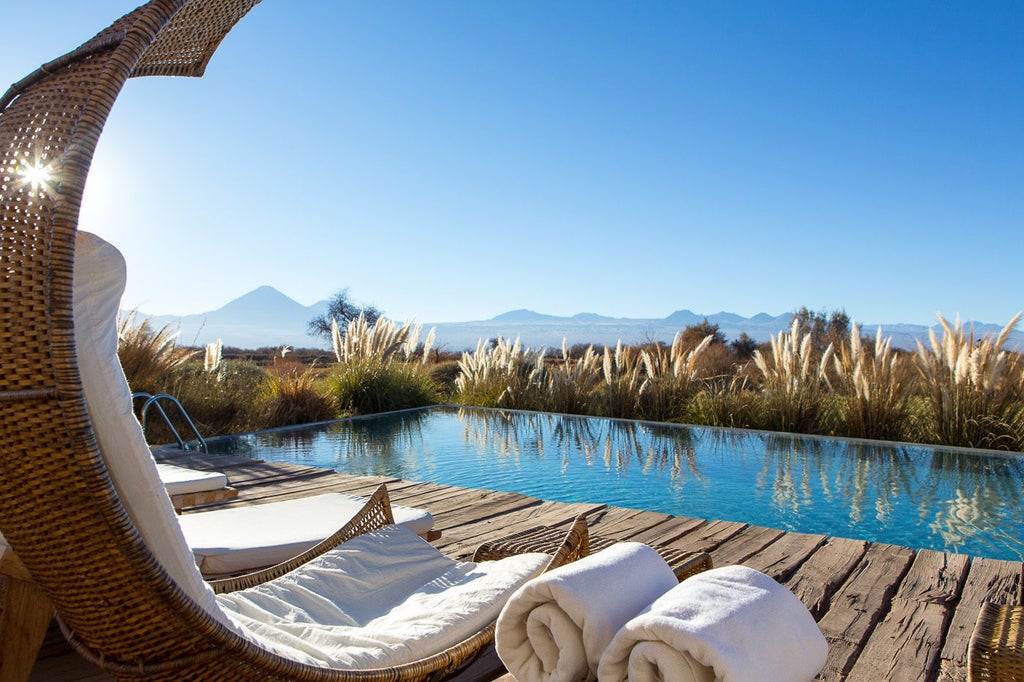 Contemporary desert resort with infinity pool reflecting Licancabur volcano, featuring modern stone architecture and Atacama desert views