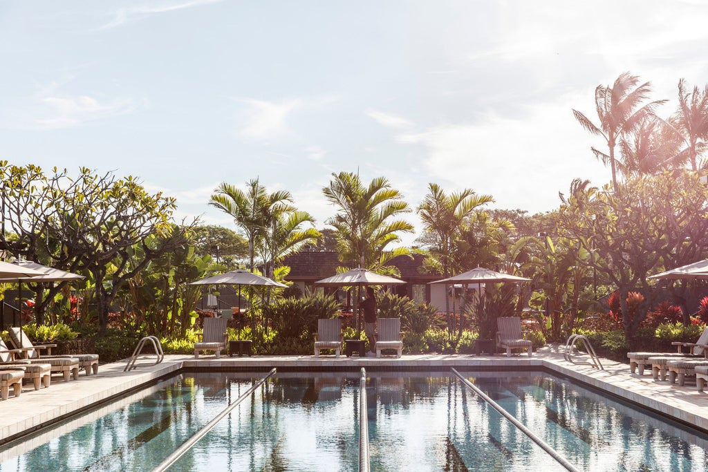 Oceanfront luxury resort with infinity pools merging into Pacific horizon, surrounded by swaying palms and black lava rock landscapes