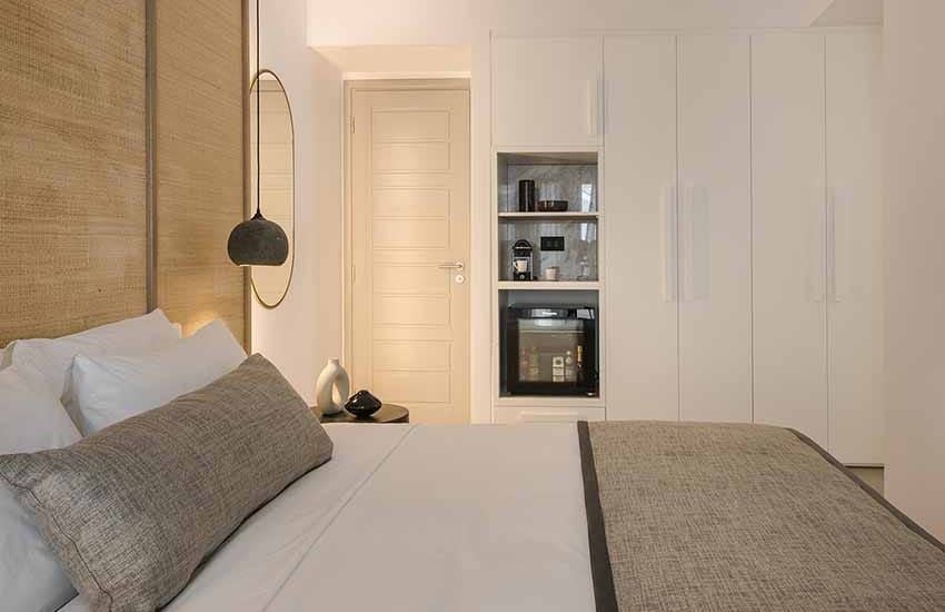 Elegant white-washed Cycladic-style deluxe hotel room with panoramic azure Aegean Sea view, minimalist design, and private balcony at luxury resort