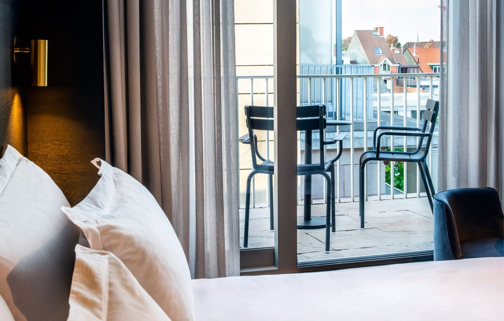 Elegant luxury hotel room with plush white bedding, decorative throw pillows, and refined neutral color palette showcasing Belgian boutique hotel design