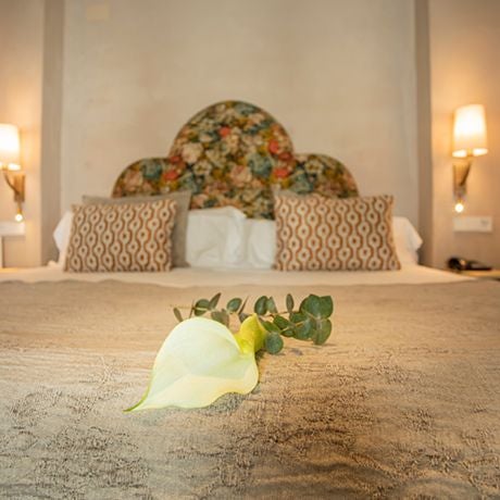 Elegant white-walled junior suite with wooden floors, minimalist four-poster bed, and traditional Spanish architectural details in Seville hotel room.