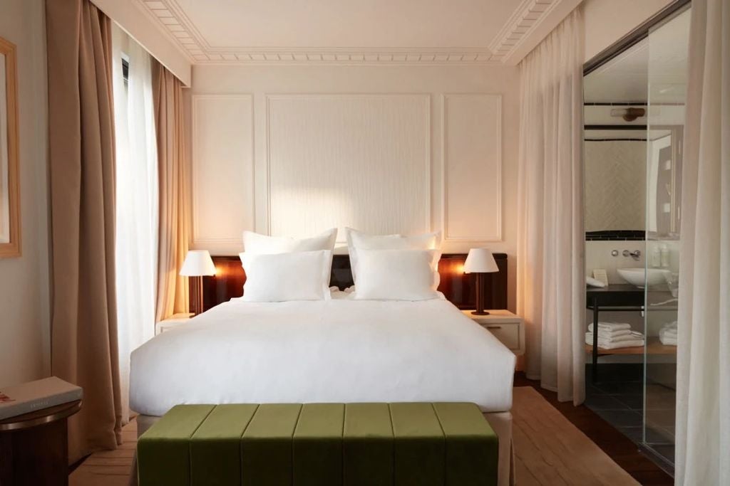 Elegant hotel room with plush king bed, floor-to-ceiling windows, modern pendant lighting, and romantic Parisian balcony views