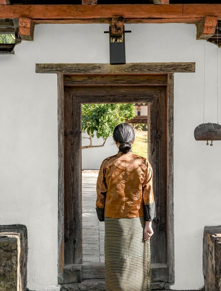 Luxurious mountain lodge with traditional Bhutanese architecture overlooking terraced rice fields and misty Himalayan peaks at sunset