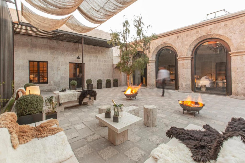 Elegant stone archways frame a colonial-style boutique hotel courtyard with potted plants, rustic wooden doors and soft evening lighting