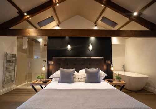 Luxurious barn-style suite with elegant rustic decor, featuring exposed wooden beams, plush bedding, and modern minimalist furnishings at countryside retreat