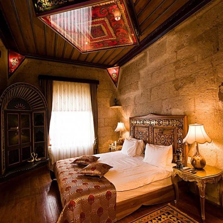 Elegant museum-themed hotel suite with ornate Turkish decor, plush king bed, vintage art pieces, and rich burgundy and gold color palette