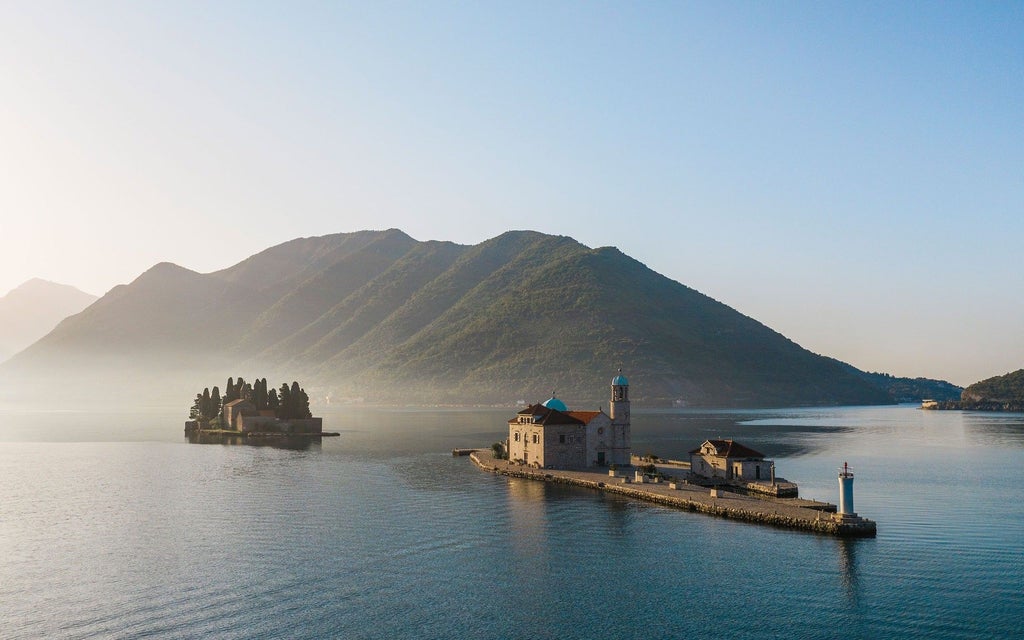 Luxurious white sailboat gliding through crystal-blue waters of Kotor Bay, with dramatic limestone mountains and medieval coastal town in backdrop