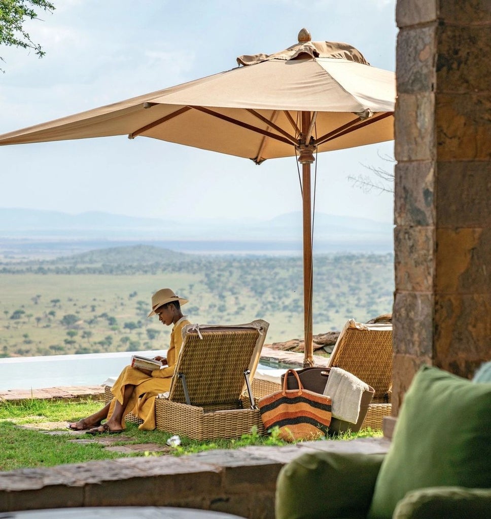 Elegant stone lodge perched on Serengeti hillside with infinity pool overlooking vast savanna plains and acacia trees at sunset