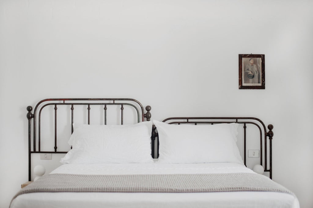 Minimalist white-washed Italian farmhouse room with natural linen bedding, stone floors, and panoramic countryside view through large window