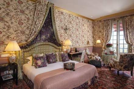 Elegant lavender-accented junior suite with pristine white linens, ornate French provincial furniture, and large windows overlooking a lush Provençal garden landscape