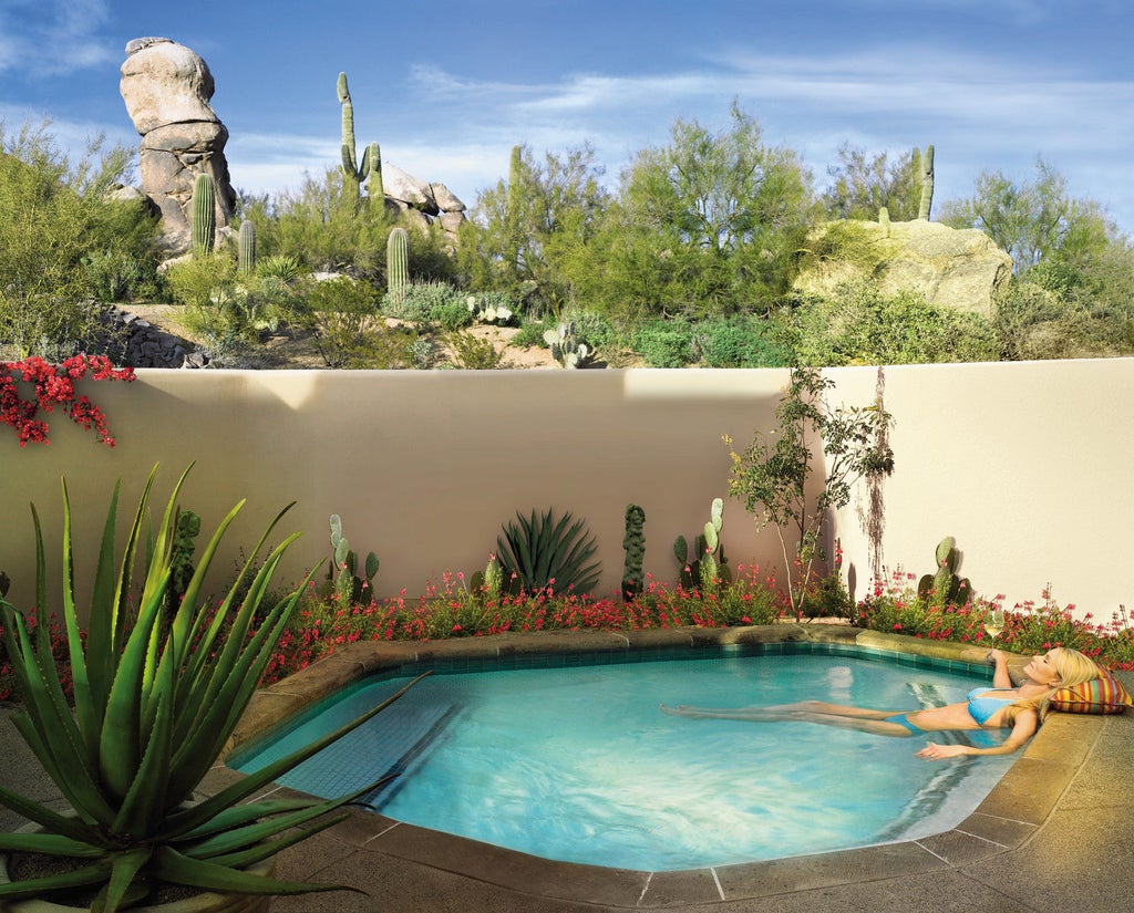 Upscale desert resort with adobe architecture nestled against red-rock mountains, featuring pristine pools and manicured cacti gardens