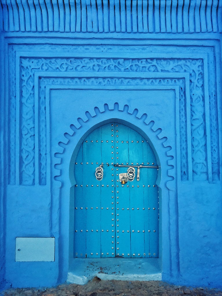 Blue-painted medina alleyway in Chefchaouen, Morocco, with intricate archways and traditional lanterns casting shadows on cobblestone path