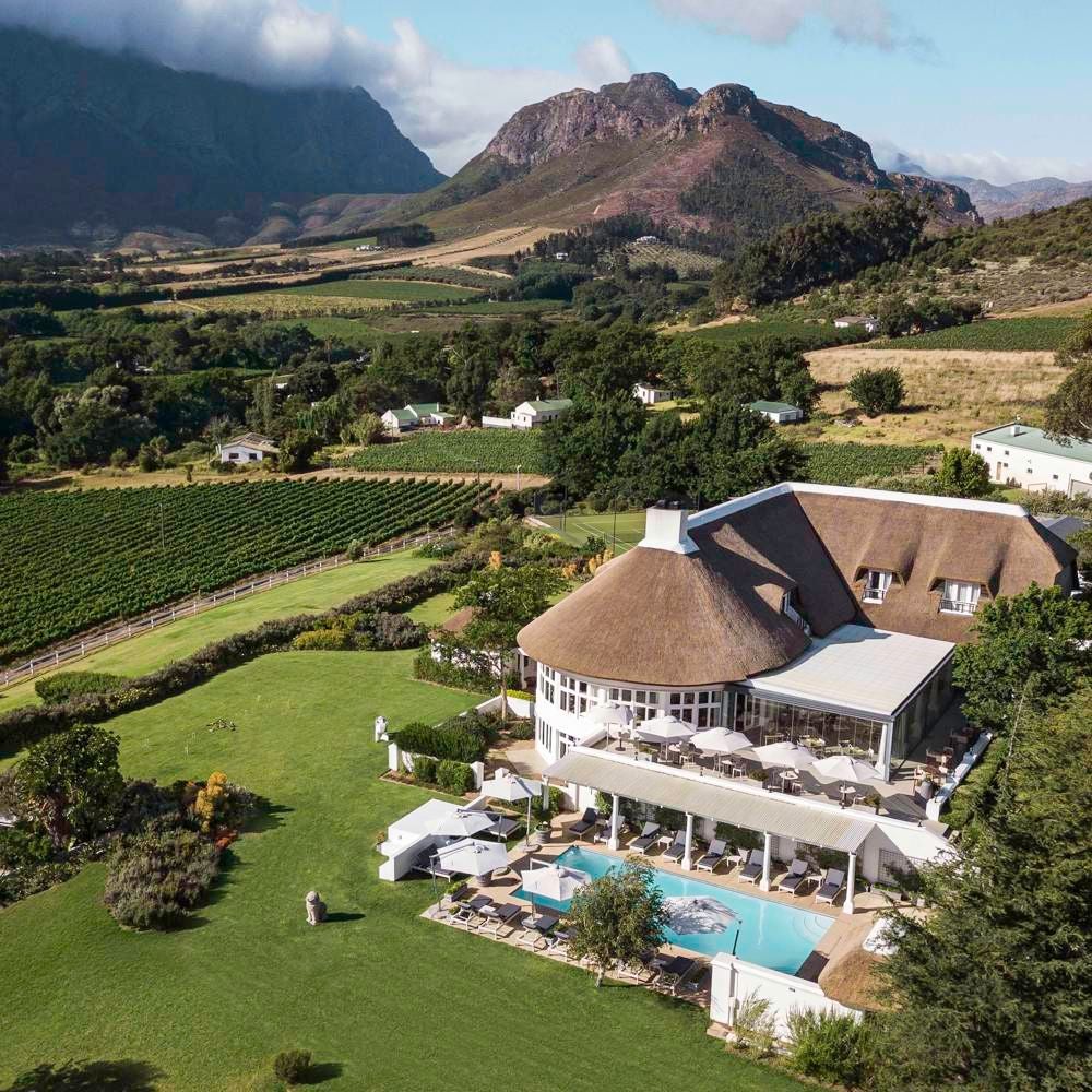 Luxurious vineyard-nestled hotel with mountain backdrop, featuring elegant stone architecture and lush green landscape in South African winelands