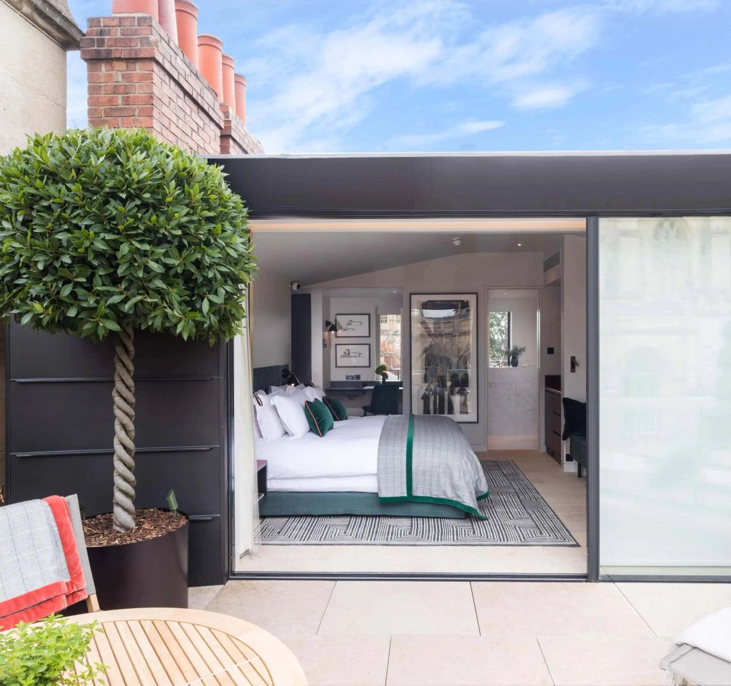 Elegantly restored historic hotel room with panoramic cityscape, vintage wooden furnishings, large arched windows revealing United Kingdom architectural landscape