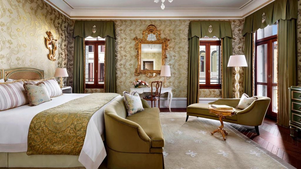 Opulent hotel room with ornate gold-framed mirrors, antique furniture, crystal chandelier and panoramic views of the Venice Grand Canal