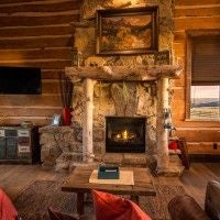 Rustic lodge bedroom with wooden furnishings, soft bedding, and large window overlooking scenic mountain landscape at a scenic ranch retreat.