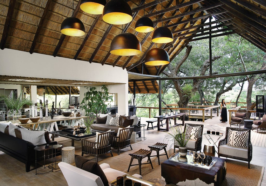 Luxurious elevated safari lodge with thatched roof and wooden deck overlooking African bushveld, sunlight filtering through trees