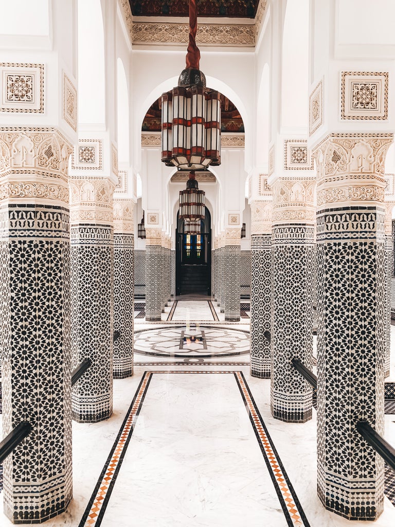 Opulent Moroccan luxury hotel La Mamounia featuring ornate archways, geometric tile work, and lush gardens under blue desert sky