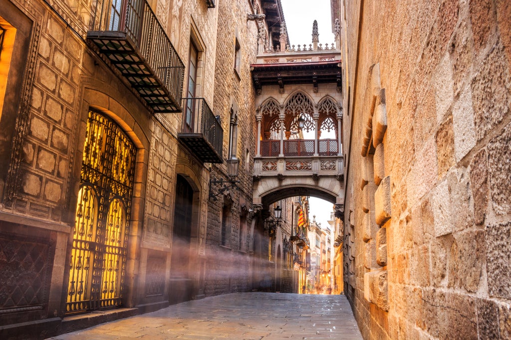 Sunlight illuminates Gothic Quarter's narrow cobblestone streets, with ornate medieval architecture and Picasso Museum's elegant facade in Barcelona, Spain