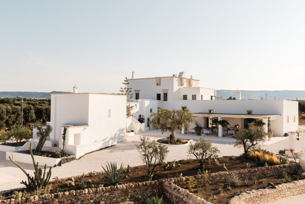 Rustic stone villa nestled in Puglia's countryside, with sun-drenched stone walls, olive groves, and elegant Mediterranean terrace overlooking rolling landscapes