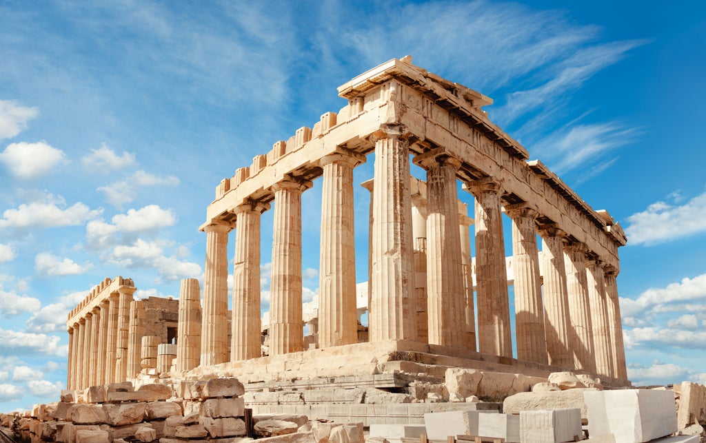 Panoramic view of Athens cityscape at sunset, with illuminated Acropolis and Parthenon atop hillside overlooking white buildings