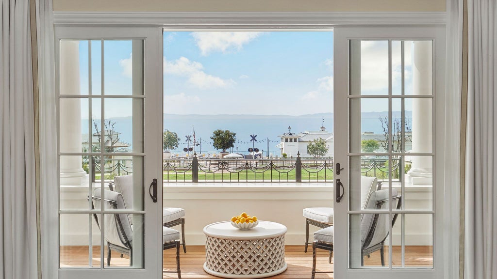 Luxurious oceanfront resort with pristine white buildings, palm trees, and elegant outdoor pool overlooking the scenic Californian coastline at sunset