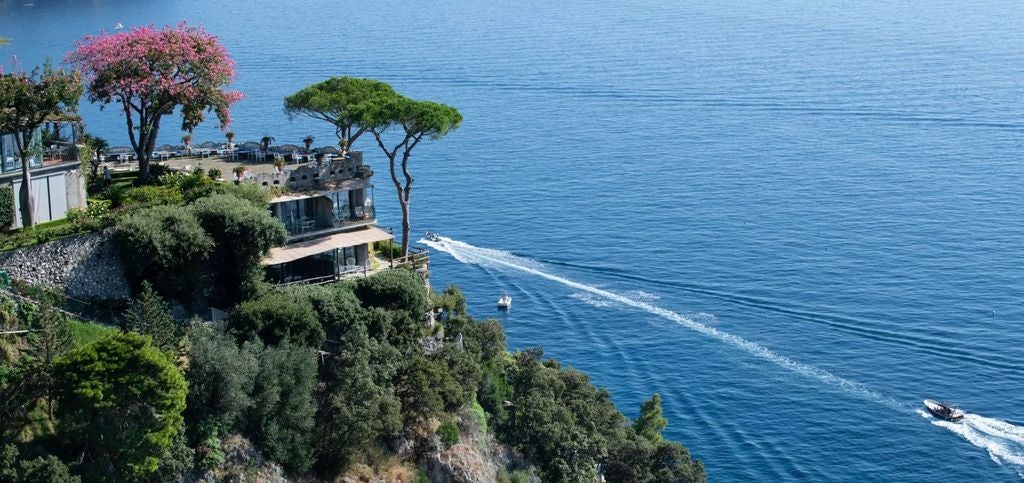 Elegant Italian luxury hotel perched on Positano cliffs, featuring tiered terraces with panoramic Amalfi Coast views at sunset