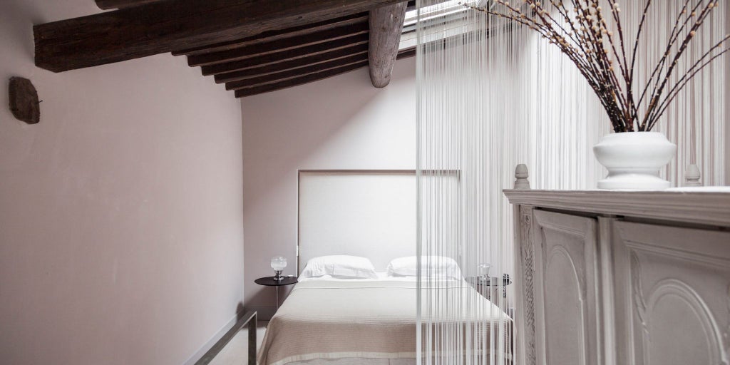 Sophisticated loft-style hotel room in Italian design with minimalist furnishings, exposed wooden beams, and soft natural lighting.