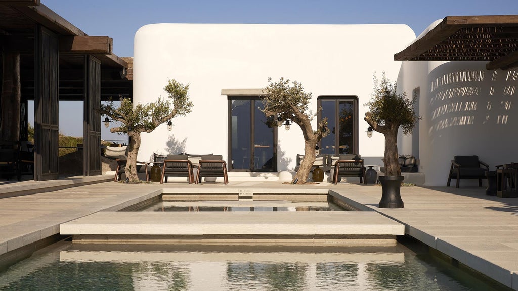 Whitewashed luxury villa with private infinity pool overlooking Aegean Sea, featuring minimalist Cycladic architecture at sunset