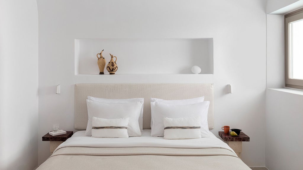 Elegant white minimalist honeymoon suite with infinity pool overlooking Santorini's azure caldera, featuring crisp linens and modern Mediterranean design