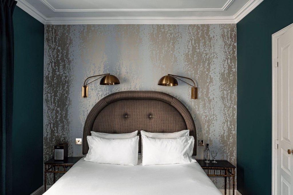 Elegant, compact Parisian hotel room with plush king bed, soft neutral tones, vintage-inspired decor, and large window overlooking charming streetscape