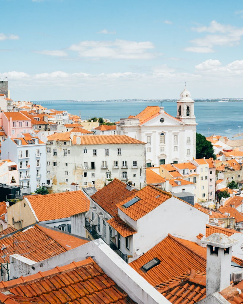 Iconic yellow tram ascending steep cobblestone street in Lisbon's historic Alfama district, framed by pastel-colored buildings and iron balconies